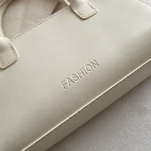 Detail van de reliëf FASHION belettering en fijn stiksel op de crème lederen handtas