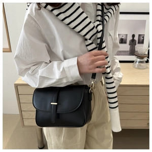 Detail of a minimalist black leather crossbody bag with a sleek gold metal bar accent
