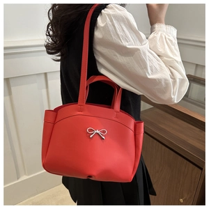 Detail view of a bright red bucket bag featuring a silver metal bow buckle and pleated sides