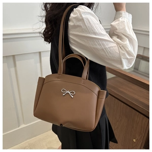 Close-up of caramel brown tote bag with silver bow accent and pleated detail on the sides