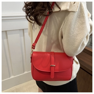 Detail showing red leather crossbody bag with gold metal clasp on a cream sweater