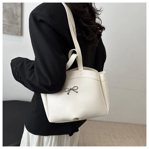 Détail d'un sac cabas crème avec nœud montrant la structure pliée et le porté à l'épaule