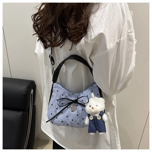 Detail of blue striped crossbody bag featuring a leather bow and cute plush bear charm