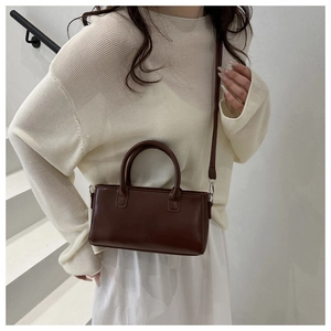 Model draagt donkerbruine vierkante crossbodytas met verstelbare riem en modelettering