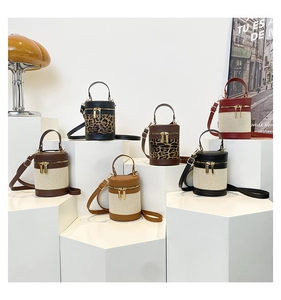 Multiple stylish cylinder shoulder bags in canvas and leather displayed on a white stand