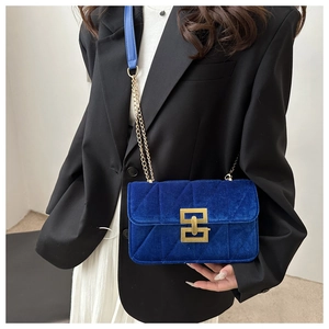 Close-up of model wearing navy velvet crossbody bag with gold chain strap and quilted pattern