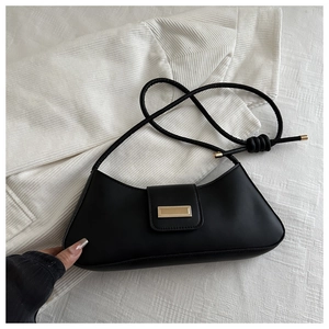 Close-up of black baguette bag with gold metal buckle on white corduroy surface