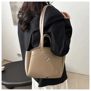 Detail of beige minimalist tote bag with silver bow accent and slim shoulder straps