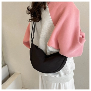 Detail view of a black crescent crossbody bag worn over a casual hoodie on a clean background