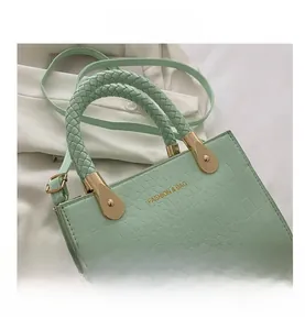 Detail of mint green crocodile pattern bag with woven handle and gold fashion lettering