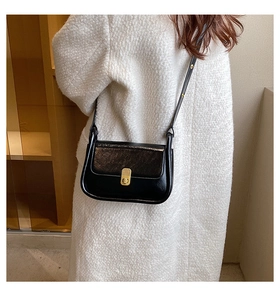 Close-up of gloss black leather crossbody bag with vintage gold clasp on a model