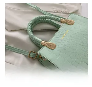 Detail of mint green crocodile pattern bag with braided handle and gold metal hardware