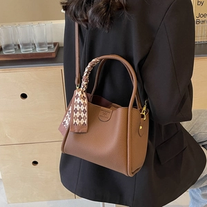 Dettaglio borsa a secchiello in pelle marrone con foulard di seta decorativo sul manico