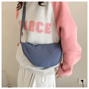 Blue canvas crescent bag worn crossbody with an adjustable strap on a female model