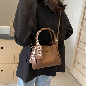 Dettaglio di borsa a secchiello in pelle litchi marrone con foulard e tracolla
