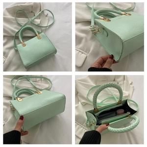 Detail view of mint green crocodile-pattern handbag with woven handles and golden hardware