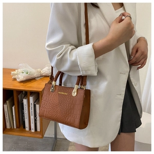 Detailed view of brown crocodile-textured handbag featuring gold accents and woven handles