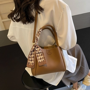 Dettaglio della borsa a secchiello in pelle marrone con foulard in seta a scacchi