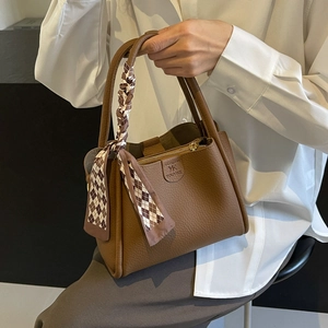 Dettaglio borsa a secchiello in pelle marrone con elegante foulard in seta a scacchi