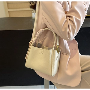 Dettaglio borsa a mano beige in pelle martellata con manico a foulard e logo inciso