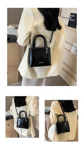 Detail of black glossy bucket bag featuring fashion logo and heart charm accessory