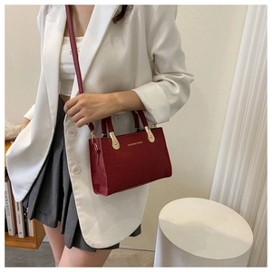 Detail of burgundy crocodile-embossed tote bag with gold fashion text and hardware