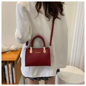 Detail of burgundy crocodile pattern crossbody bag with golden hardware on a white blazer