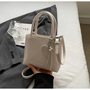 Detail of cream white faux leather bucket bag with top handles and a heart charm