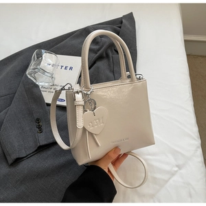 Detailed shot of cream white bucket bag with heart charm and silver fashion logo