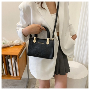 Detail of black crocodile pattern tote bag with woven handle and gold hardware on model