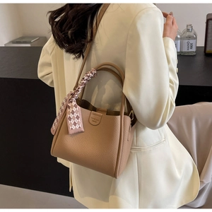 Dettaglio borsa a secchiello in pelle marrone con foulard in seta su un blazer bianco