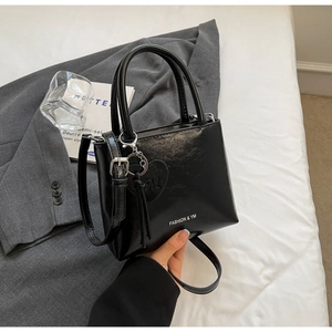 Detail of a chic black glossy bucket bag with heart tassel and detachable shoulder strap