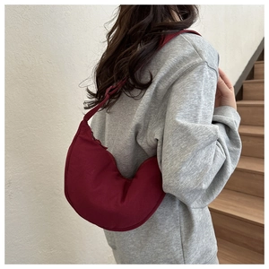 Detail view of a burgundy half-moon crossbody bag with wide shoulder strap