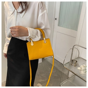 Detail of yellow crocodile pattern handbag featuring a woven handle and gold hardware