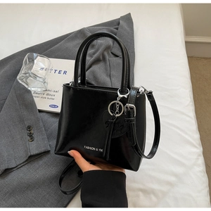 Detail of black glossy bucket bag with heart pendant and adjustable strap on a white surface