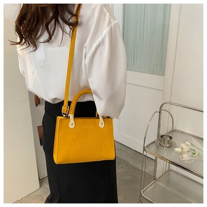 Detail of yellow crocodile embossed handbag featuring a woven top handle and metal hardware