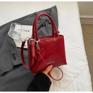 Detailed view of red patent leather bucket bag with heart pendant on white bedding