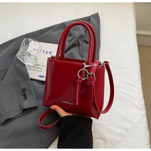 Detail of red glossy leather handbag with fashion logo and heart charm chain strap