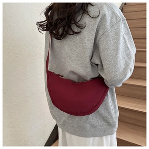 Deep red crescent crossbody bag with adjustable wide strap shown on a model on stairs