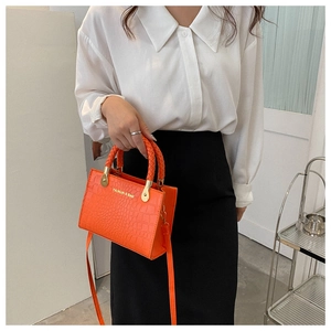 Detail of orange crocodile embossed tote bag featuring a woven handle and gold logo