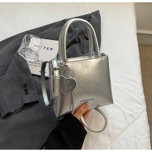 Detail of silver metallic textured crossbody bag with heart pendant on grey blazer