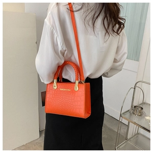 Close-up of orange crocodile pattern PU leather bag with woven handle and gold hardware