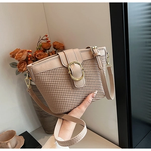 Detail of beige woven bucket bag with gold ring buckle and adjustable leather strap