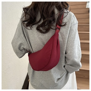 Rear view of a model wearing a burgundy half-moon nylon crossbody bag on a shoulder