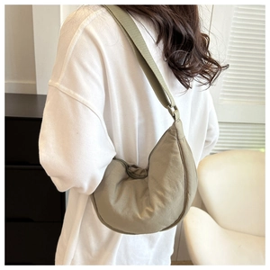 Sage green crescent crossbody bag shown on model in a minimalist indoor setting