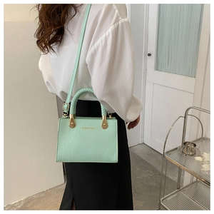 Detail of mint green crocodile pattern bag featuring a woven handle and gold-tone hardware