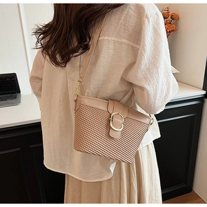 Detail of apricot woven crossbody bag with gold buckle on a shoulder-slung model