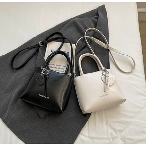Detail of chic black and cream bucket bags with metal heart charms on a grey blazer