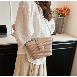 Macro view of woven lattice texture and golden metal clasp on soft pink crossbody bag