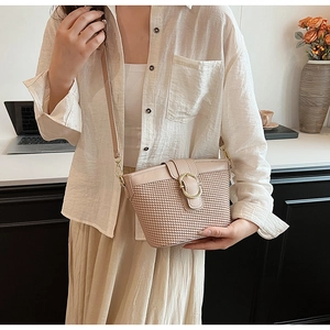 Detail of light beige woven crossbody bag with gold buckle shown on a model